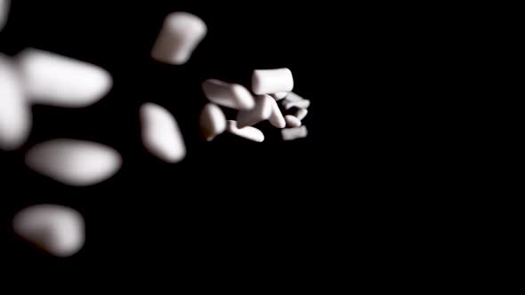 Pieces of White, Minty Chewing Gum Falling into Black Background alt