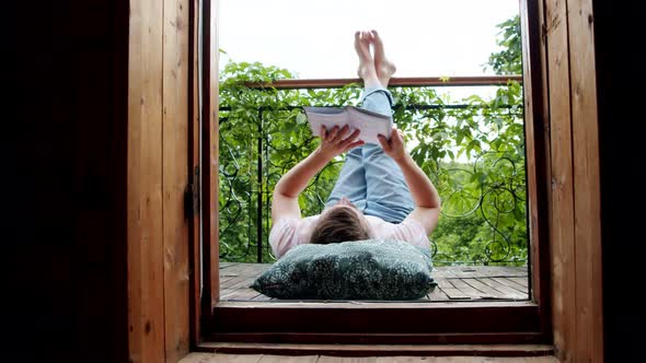 a Man Lies on His Balcony and Reads a Book with His Legs Up alt