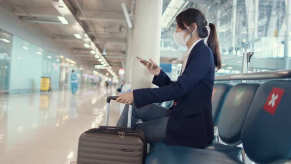 Asian business lady traveller wear suit sitting with suitcase and use smart phone chat message.