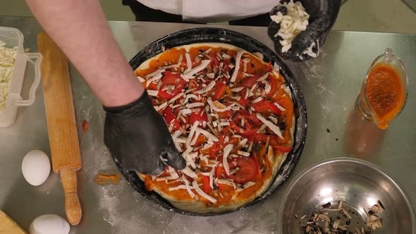 Close-up of the Chef Sprinkling Freshly Baked Pizza with Cheese in the Kitchen. alt
