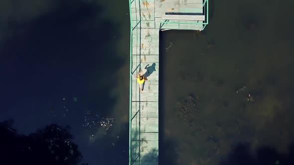 Little boy walking on the long wooden bridge and jumping into the water in a sunny day. alt