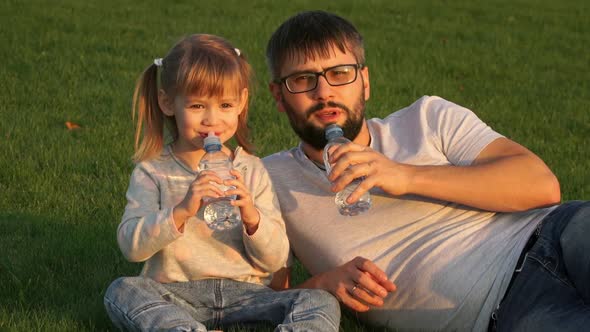 Father with Child Girl Look at Camera Smile Laugh and Drink Natural Water From Bottle Outdoors
