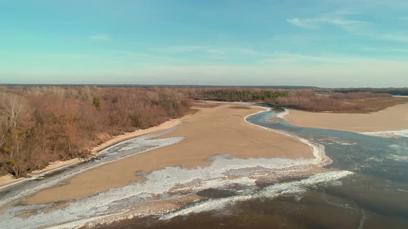 Aerial Drone Footage of Flight Over a Sandy Shore with a Small River in Winter