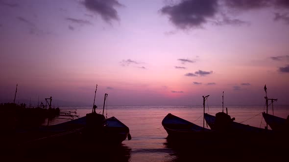 Sunset on beach with long tail fishing boats moored to coastline. Pink sky, clouds. Phangan Thailand