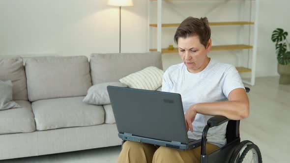 Mature 50 Years Female Freelancer is Working Typing in Laptop Sitting in Wheelchair at Home alt