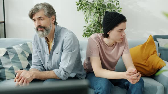 Portrait of Unhappy Family Father and Son Sitting on Couch Back To Back in Silence alt
