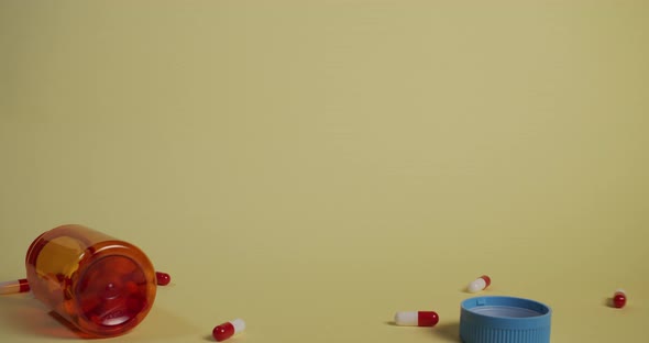 Slow motion wide shot of a bottle of pills falling, the lid flies off and pills shoot out. alt