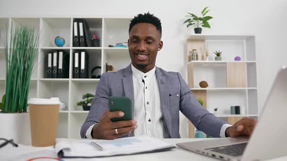 African american office manager sitting at his workplace and using smartphone  alt