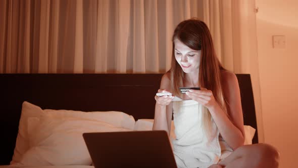 Happy Young Woman Holding Credit Card Using Instant Mobile Payments at Home alt