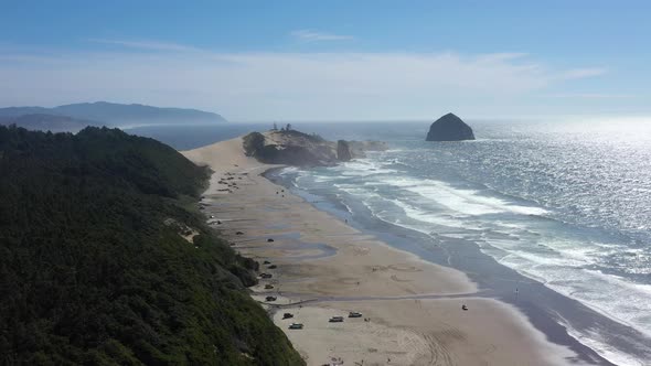 Flying above the beach full of people toward Chief Kiawanda Sea Stack Rock near Pacific City, Oregon alt