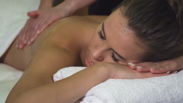 Cropped Shot of the Face and Back of a Girl Who Has a Back Massage in the Spa Salon alt