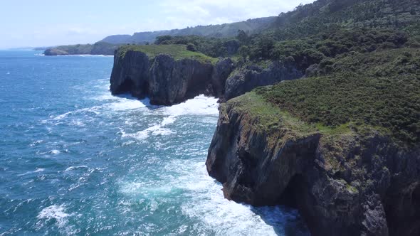 ocean waves crash into large coastal cliffs in Asturias Spain on bright sunny day alt
