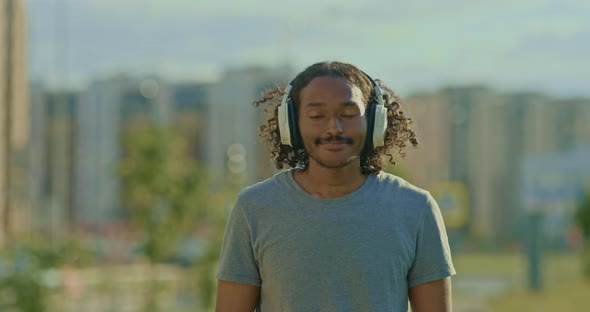Happy African American Man Walks Around the City in Headphones Listens to Music