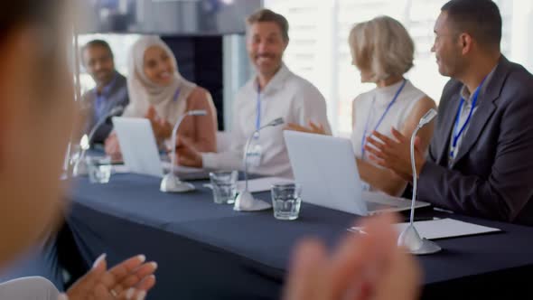 Audience and panel of business delegates applauding businessman at a conference alt