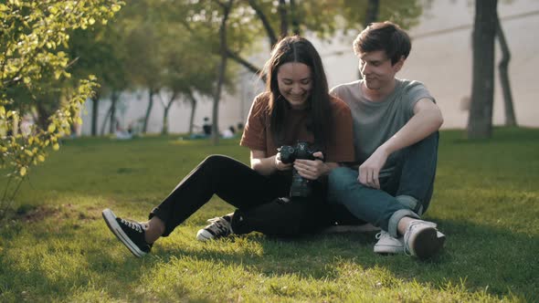 A couple in love on a date. A girl and a guy sit on the grass and look at the photos on the camera.
