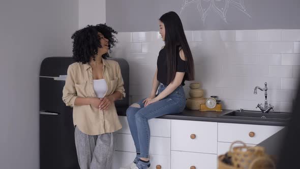 Two Young Female Friends Standing in Kitchen Gossiping alt