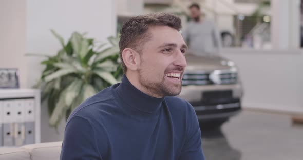 Close-up Face of Handsome Caucasian Man Sitting in Car Dealership and Smiling alt