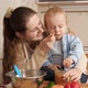 Cute Baby Boy Sitting on Kitchen Table and Playing with Cookware While Mother Feeding Him with - VideoHive Item for Sale