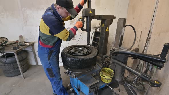 Technician Worker Takes Off the Tire From the Wheel in Garage alt