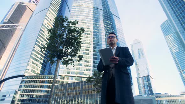 Male Manager Is Walking Along the Business Complex Composed of Skyscrapers alt