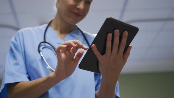Midsection of portrait of caucasian female doctor using digital tablet in hospital room alt