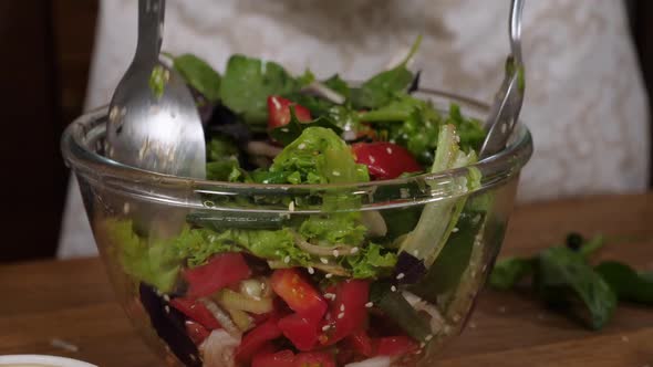 Woman Mixing Fresh Salad in Class Bowl, Close-up. alt