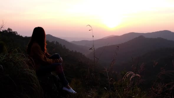 Slow motion of a female traveler sitting on the mountain peak and watching sunrise in the morning