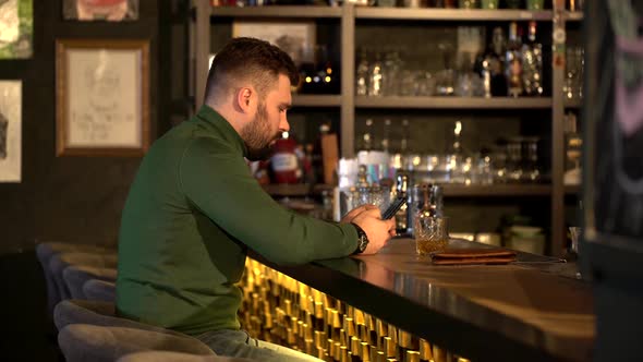 Guy Sits at Bar Counter with Glasses of Alcohol.