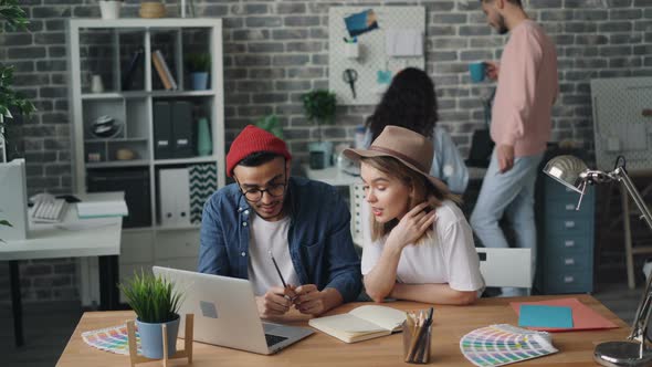 Man and Woman Working Together Looking at Laptop Screen Sitting in Office alt