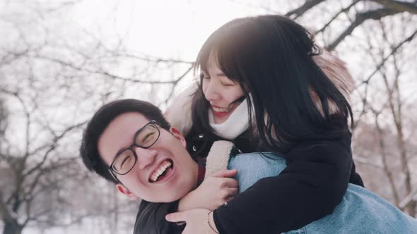 Young Man Giving Piggyback Ride To His Girlfriend in the Park on Snowy Winter Day alt