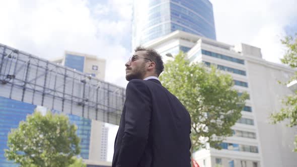Businessman walking against high-rise business centers. alt