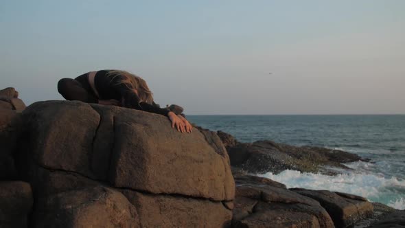 Young Woman in Black Tracksuit Stretches on Grey Rocky Cliff alt