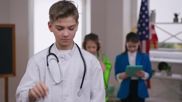 Serious Teenage Boy Putting on Coronavirus Face Mask Gesturing Thumb Up Looking at Camera alt