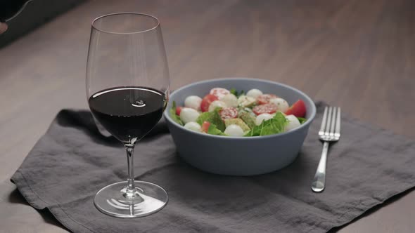Slow Motion Pour Red Wine Into Wineglass with Bowl of Salad on Background alt
