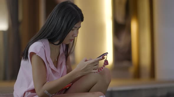 A Girl Looking Sad While Using Mobile Phone Sitting on the Floor alt