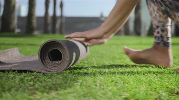 Woman Hands Rolling Up Yoga Mat After Training in park.Girl Folding Mat on Grass alt