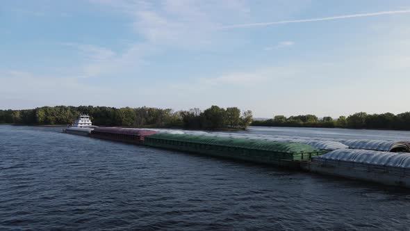 Tub boat pushing empty barges up the Mississippi River on a bright blue summer day. Trees on islands