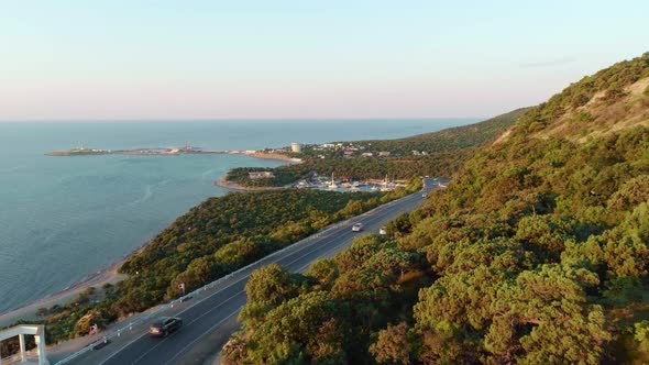 The camera flies over cars driving along a winding road amongst the mountains and the seashore