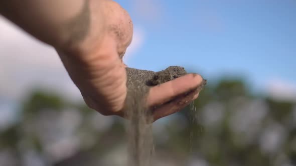 close-up hand grabs a handful of dry sand and lets it fall between his fingers alt