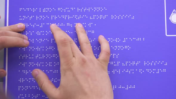 Hands of a Blind Man in a Shirt Reading a Braille Font on a Building Sign alt