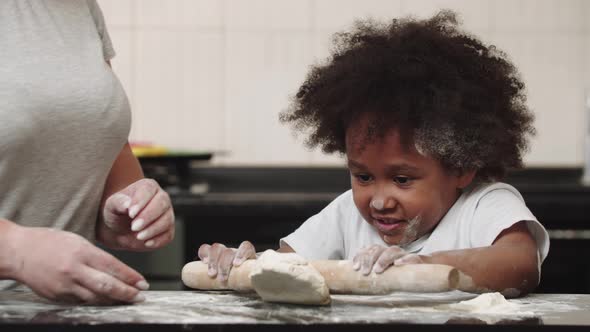 Black Little Girl with Her Mother Rolling Out the Dough in the Kitchen alt