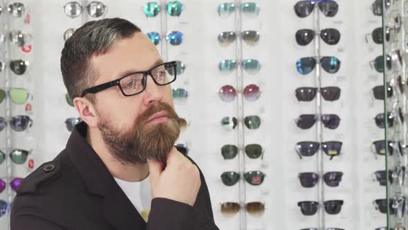 Bearded Mature Man Rubbing His Beard Thoughtfully Choosing New Glasses alt