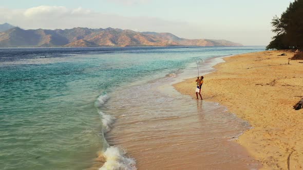 Single guy catching fish on marine coast beach wildlife by clear sea with white sandy background of  alt