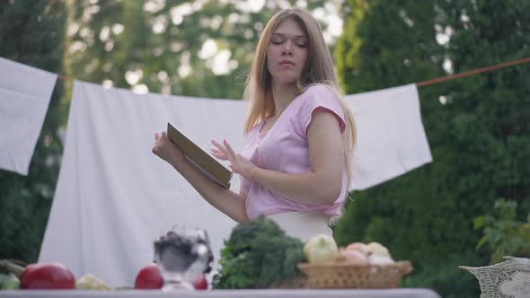 Side View Confident Slim Young Housewife Reading Recipe Looking at Ingredients on Table on Backyard alt