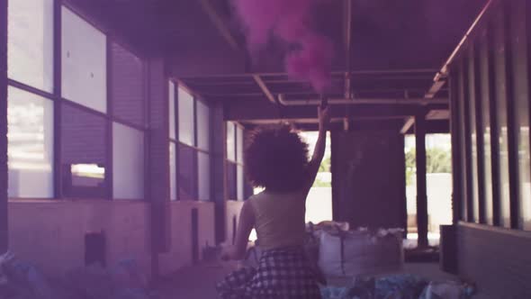 Mixed race woman holding purple flare running through an empty building alt