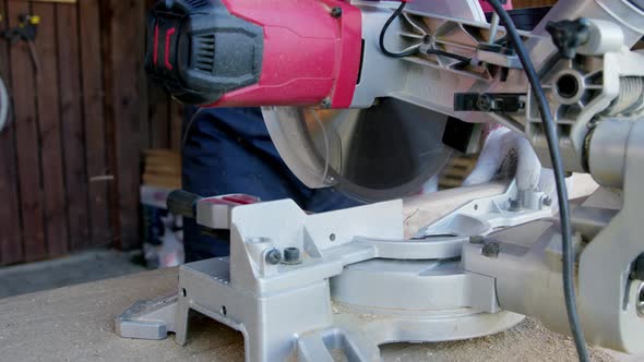 Male Carpenter in Gloves Cuts Off Wooden Workpiece on Mitre Saw Close-up alt