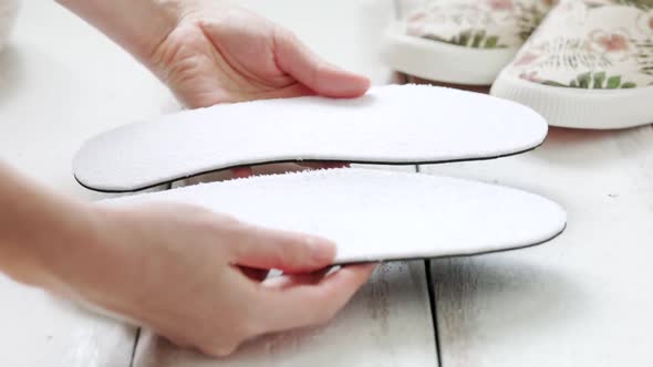 Woman's hands hold orthopedic insoles for shoes, comparing them with each other. alt