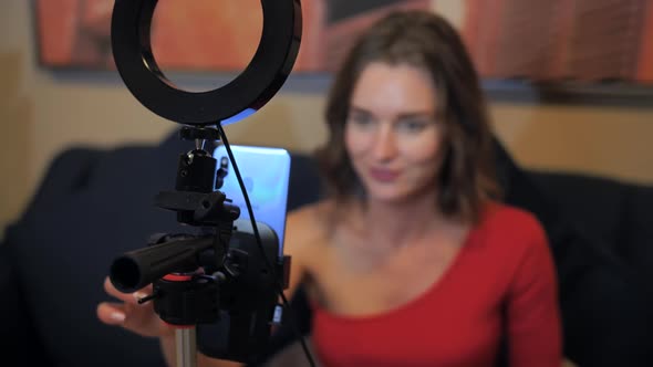 A Beautiful Girl in a Red Dress is Broadcasting Live at Home Using a Smartphone alt