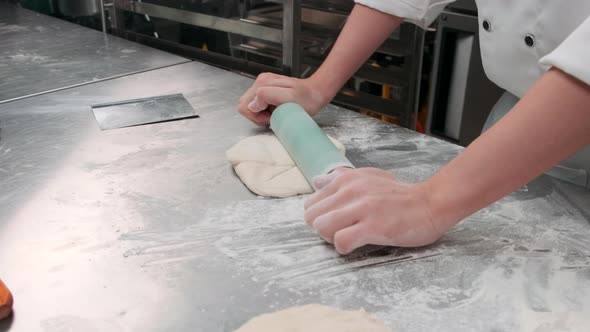 Chef is preparing pastry dough, baking bakery food on a stainless steel table.