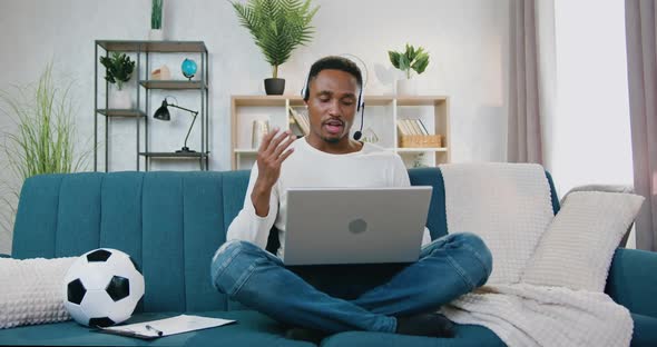Man in Headset which Sitting on the Couch at Home and Holding Video Meeting on Laptop alt